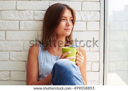 Caucasian girl in pensive mood and with thoughtful facial expression drinking a cup of coffee in the morning