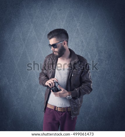 A handsome fashion model with beard standing in front of fancy background and making funny faces while using a vintage camera concept
