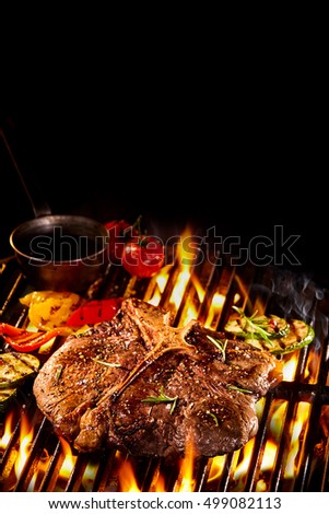Well done T bone steak on flaming barbecue grill with roasted vegetables, oil and copy space