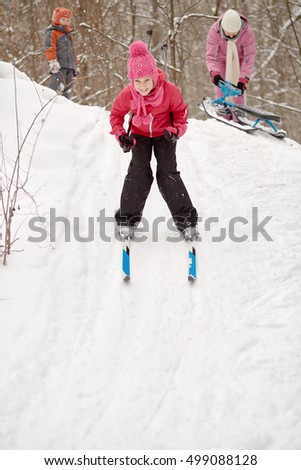 Smiling girl slides down from hill in winter park.