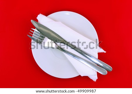 Table serving-knife, fork  and silk napkin on red   background.