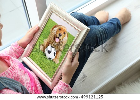 Little girl holding photo frame with picture of dog. Happy memories concept.