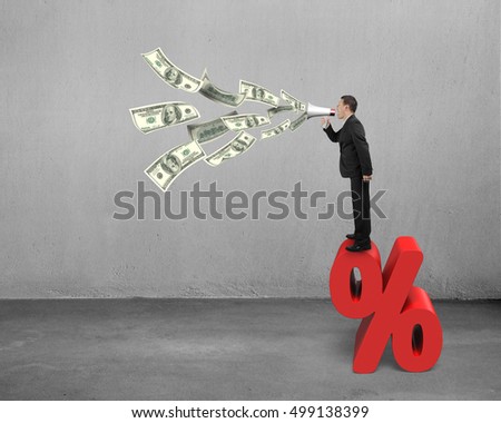 Man hold megaphone with dollar bills spraying out on red percentage sign, in concrete room background.