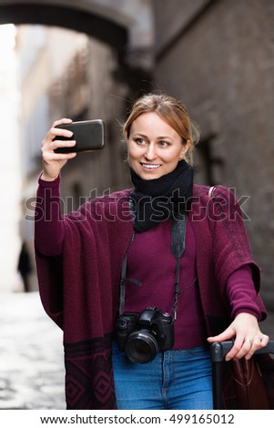 Cheerful smiling girl taking picture with her phone in the town