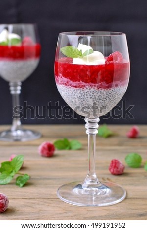 Pudding from chia seeds and raspberries with cottage with mint in glass on brown wooden background, front vertical view
