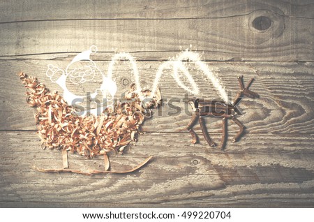 Simple symbols of Father Christmas sleigh arranged from sawdust and reindeer made from dry wooden sticks on wooden grey background.