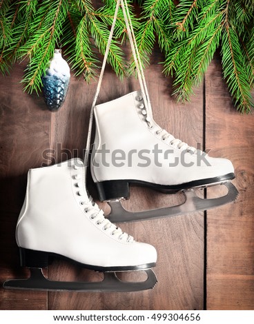 Christmas decoration. White ice skates for figure skating and fir branch on a wooden background. 