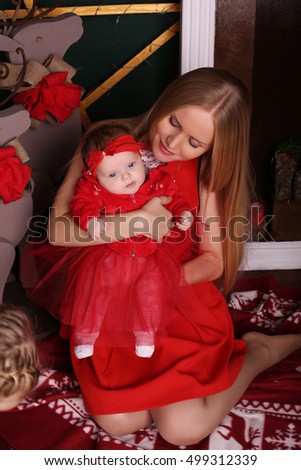 tender photo of beautiful mother with luxurious blond hair posing with her cute little baby girl beside Christmas tree in cozy home  