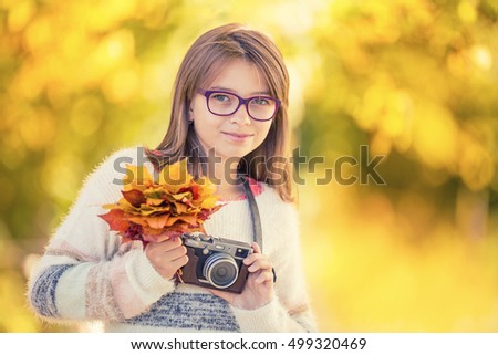 The cute young girl with autumn bouquet and retro camera.