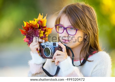 The cute young girl with autumn bouquet and retro camera.