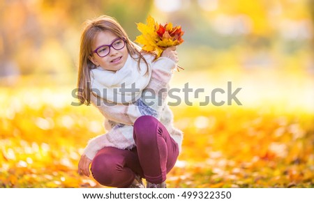 Portrait of a smiling young girl who is holding in her hand a bouquet of autumn maple leaves. Pre-teen young girl with glasses and teeth braces.