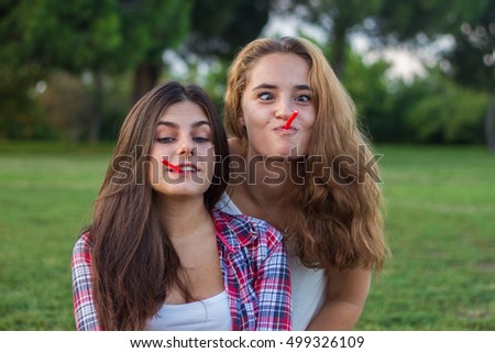 Female friends enjoying while eating red licorice a holiday in the park. They are young, one has blue eyes and the other is blonde. 