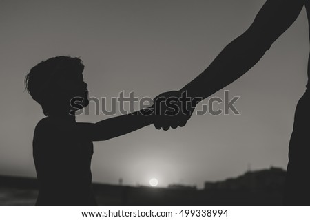 Back side view silhouettes of father holding his child hand over sunset background. Book cover idea design