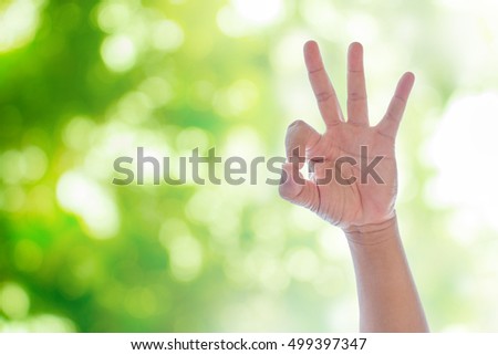 Hand action ok on green natural bokeh blurred abstract background.