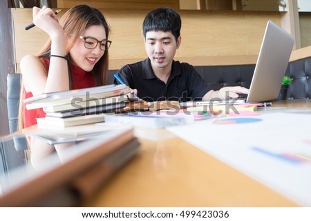 Side view of two young adult students studying and talking about lessons comparing together laptop information in a coffee shop.