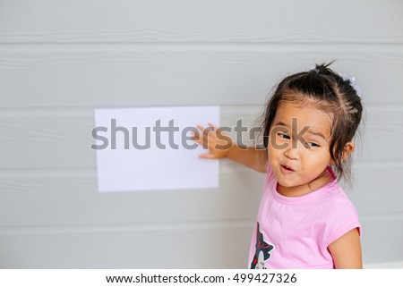 Portrait of a young asian little girl holding a blank sign white paper on wood gray background