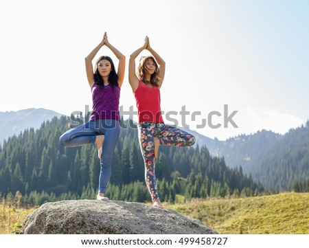 Two young women doing yoga on a rock, on a background of mountains