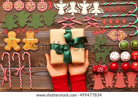 Woman holding christmas present over wooden background with homemade gingerbread cookie and handmade decoration on it 