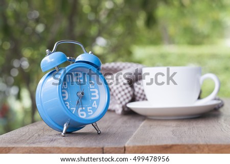 Morning coffee with alarm clock on wooden table in garden.