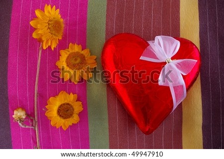 Valentine chocolate heart in red foil with white bow and flowers on pillow