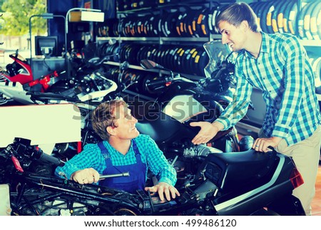 Young smiling man customer asking technician about motorcycle at service point