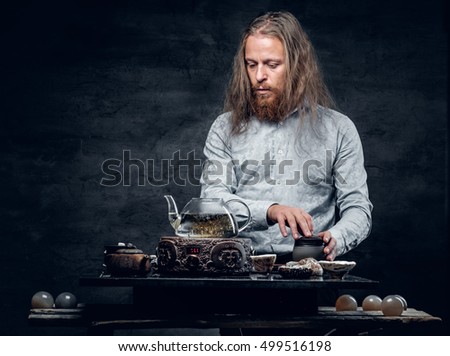 Bearded male with long hair preparing tea in Asian style.