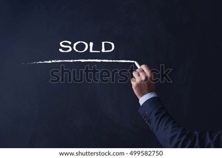 Businessman writing SOLD on Blackboard