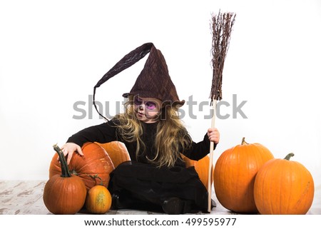 Terribly serious and dangerous witch, a girl dressed  for halloween holiday and the pumpkins.