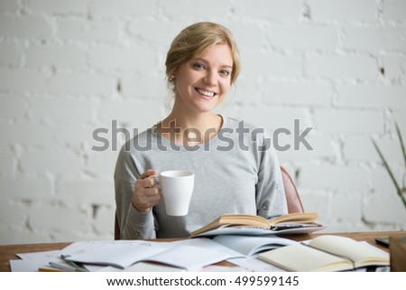 Portrait of a smiling student girl sitting at the desk with a mug in her hand, education concept photo. Looking at the camera