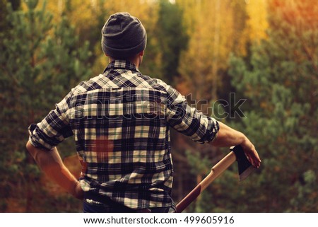 Lumberjack in checkered shirt and ax at the forest Royalty-Free Stock Photo #499605916