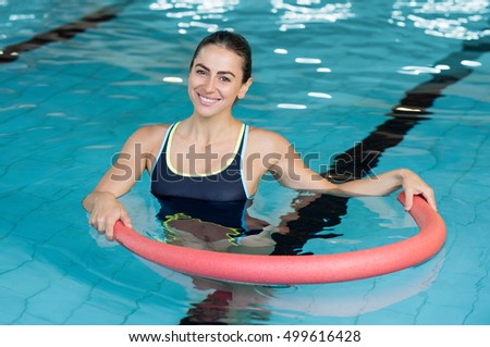 Happy smiling woman doing exercise with aqua tube in a swimming pool. Young sportive woman exercising in swimming pool with the help of a tube. Young heallthy woman doing aerobics in swimming pool.
 Royalty-Free Stock Photo #499616428