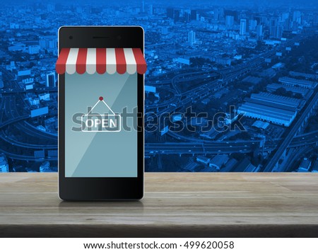 Modern smart mobile phone with on line shopping store graphic and open sign on wooden table over city tower and expressway