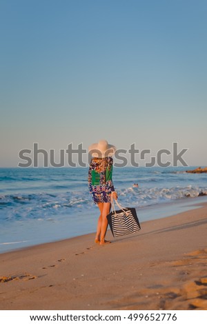 Back side view of woman in summer hat and beach bag walking on the sunny ocean tropic outdoors background