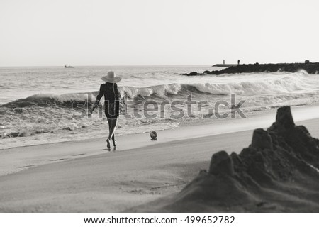 Back side view of woman in summer hat and beach bag playing ball on the sunny ocean tropic outdoors background