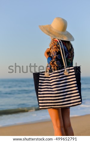 Back side view of woman in summer hat and beach bag standing on the sunny ocean tropic outdoors background