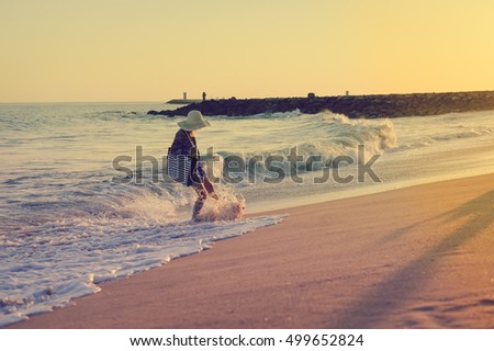 Back side view of woman in summer hat and beach bag playing with waves on the sunny ocean tropic outdoors background