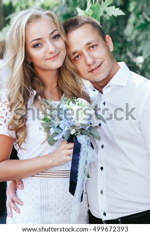 Young man leans to woman's shoulder while she holds blue wedding bouquet