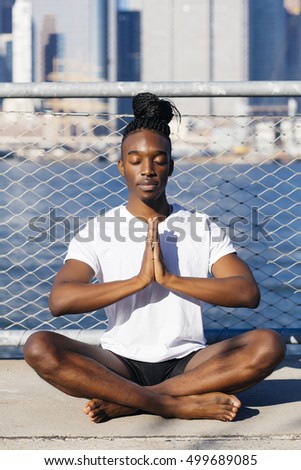 Young afroamerican man sitting in meditation outdoors, in New York city.
