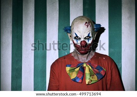closeup of a scary evil clown wearing a dirty costume, with the circus tent in the background