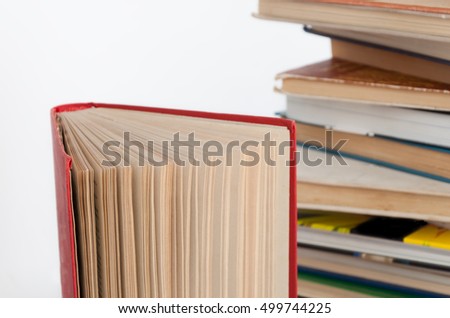 Stack of hardback books and old open book on white wall background. Search for relevant and necessary information in a large number of sources during studies or work.