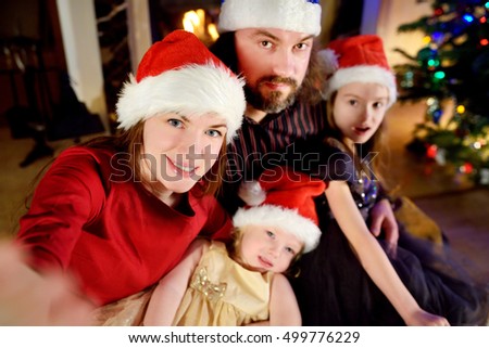 Young happy family of four taking a photo of themselves by a fireplace in a cozy dark living room on Christmas eve
