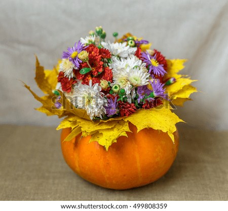 Pumpkin Vase with a bouquet of flowers and yellow leaves against the backdrop of a bright fabric