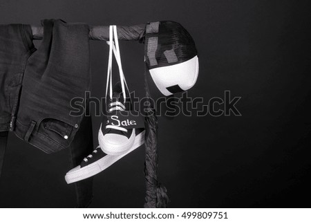 Sale sign. Black and white sneakers, cap and pant, jeans hanging on clothes rack on black background.  Black friday. Copy space.