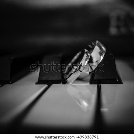 Black and white picture of wedding rings lying over the piano keys