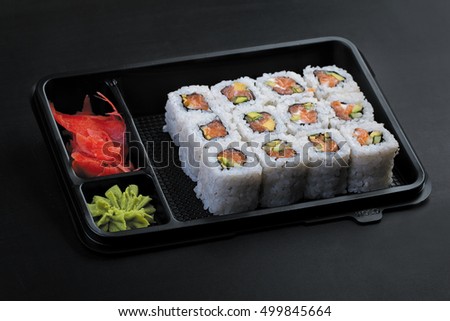 Set salmon rolls in a plastic plate on a black background