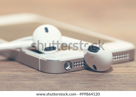 Smartphone and headphones lying on a wooden table with shallow depth of field.