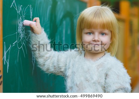 Cute child drawing with chalk on blackboard outdoor