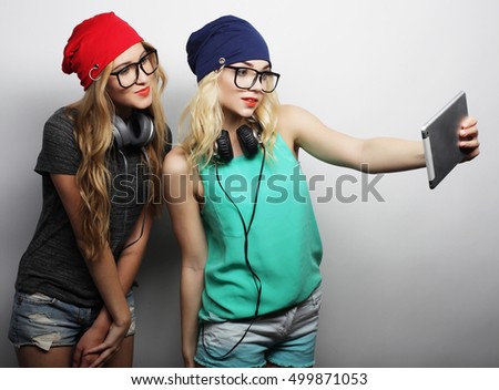 two hipster girls friends taking selfie with digital tablet, studio shot over gray vackground