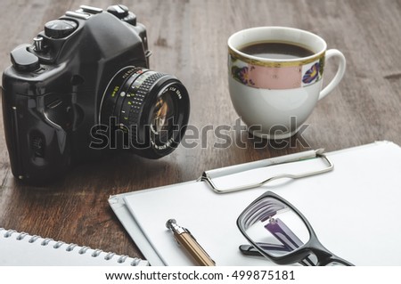 Vintage camera and coffee cup on wood table. Glasses and pen on paper