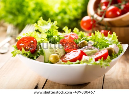 bowl of salad with vegetables and greens on wooden table Royalty-Free Stock Photo #499880467